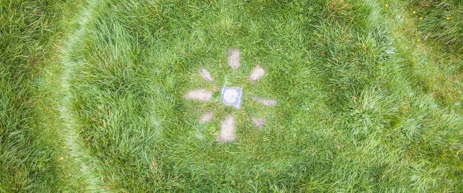 A detailed top-down aerial view focusing on the center stone plaque and radiating path markers inside the grass labyrinth