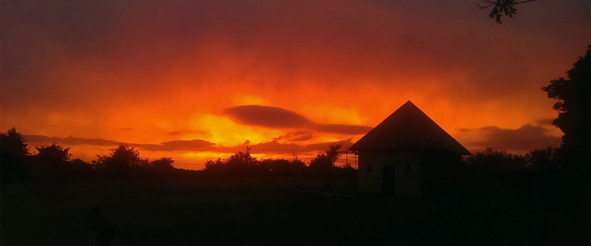 Wide landscape view of the cozy wooden healing cabin silhouetted against a dramatic evening dusk sky in Limerick