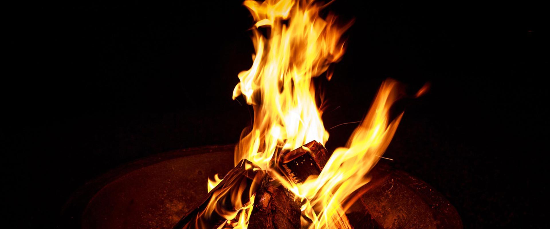 A wide panoramic view of a sacred campfire burning brightly during an evening holistic wellness ceremony
