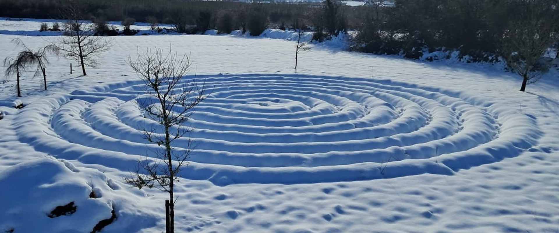 A wide panoramic view of the outdoor sacred snow labyrinth covered in winter snow at the retreat