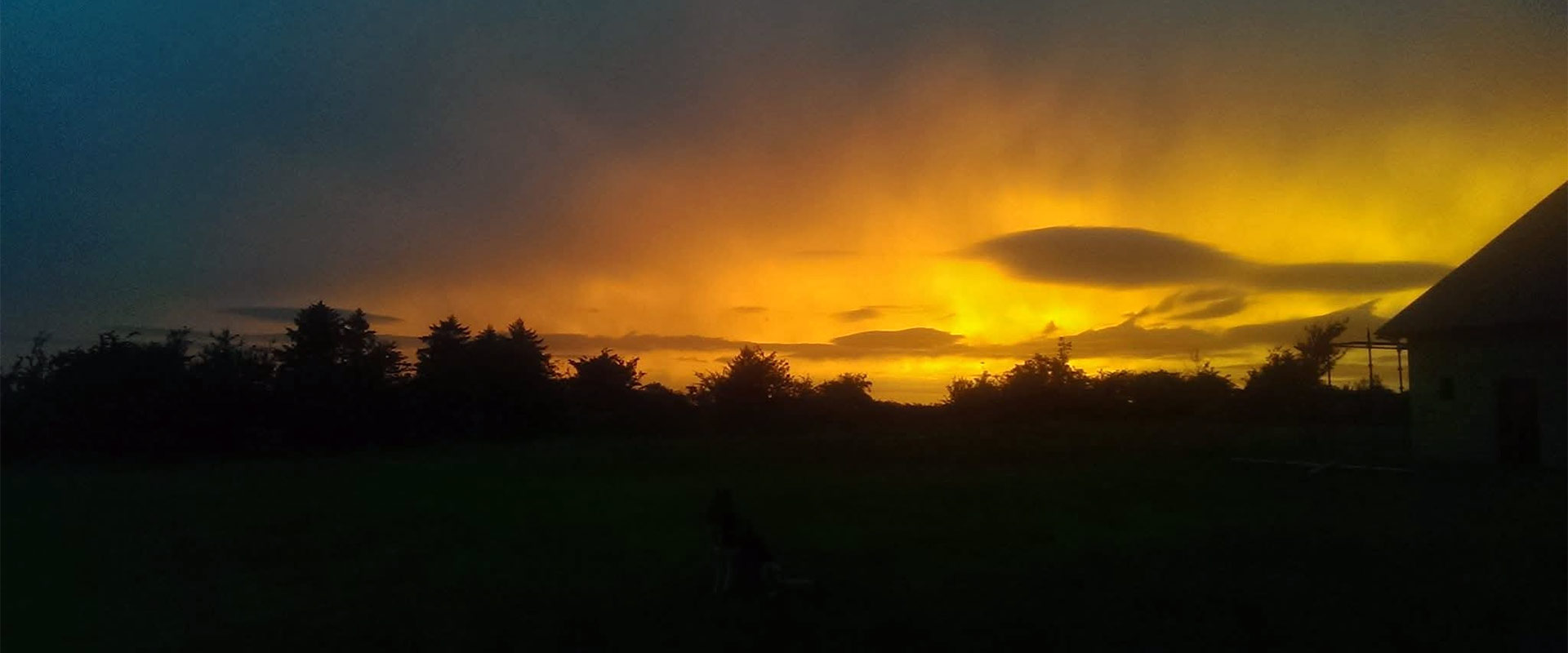 A wide panoramic view of a golden sunset over the dark horizon and quiet fields of the Earthkeepers holistic healing sanctuary
